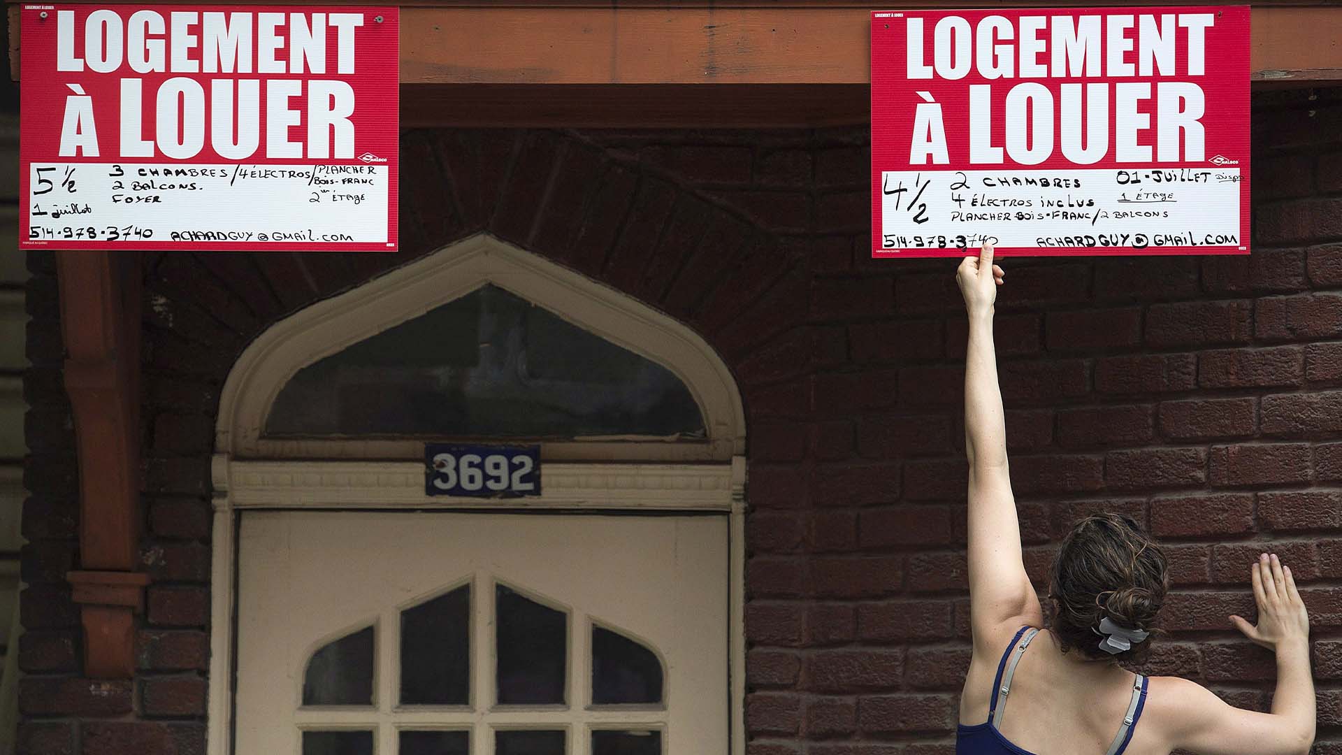 Une femme tend la main pour retirer une enseigne à louer à Montréal, le mardi 1er juillet 2014.