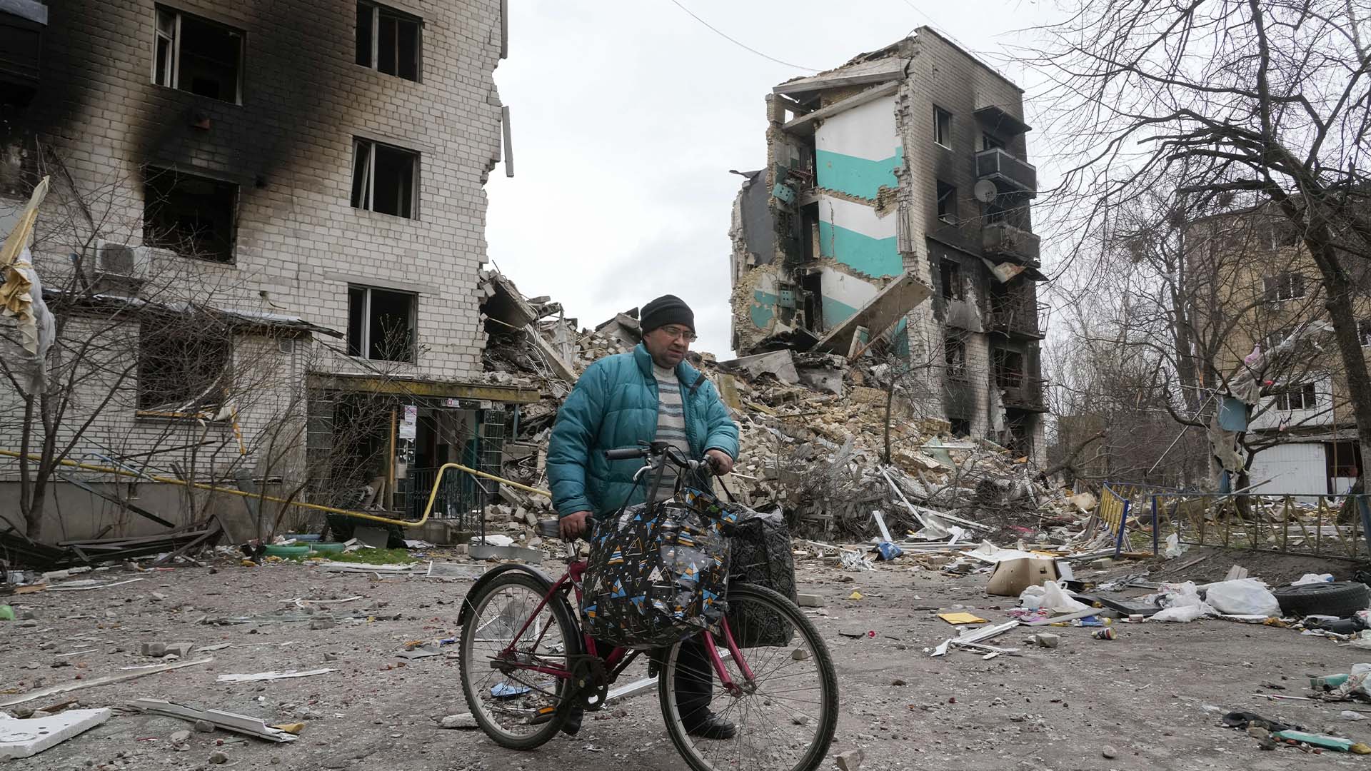 Un homme transporte ses affaires sur un vélo alors qu'il quitte sa maison, en arrière-plan, ruinée par les bombardements russes à Borodyanka, en Ukraine, le mercredi 6 avril 2022.