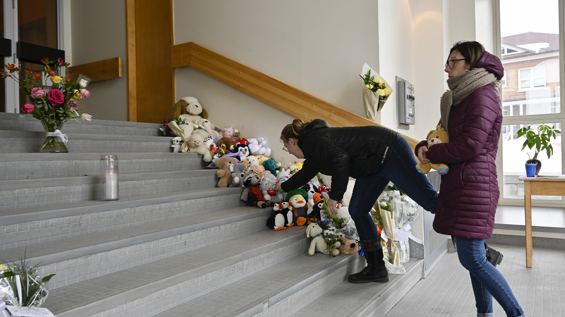 Des femmes placent des jouets en peluche sur les marches de l'église d'Amqui, au Québec, le mercredi 15 mars 2023. Deux personnes ont été tuées et neuf autres ont été blessées lundi après-midi lorsqu'une camionnette a percuté des piétons qui marchaient le long d'une route à Amqui.