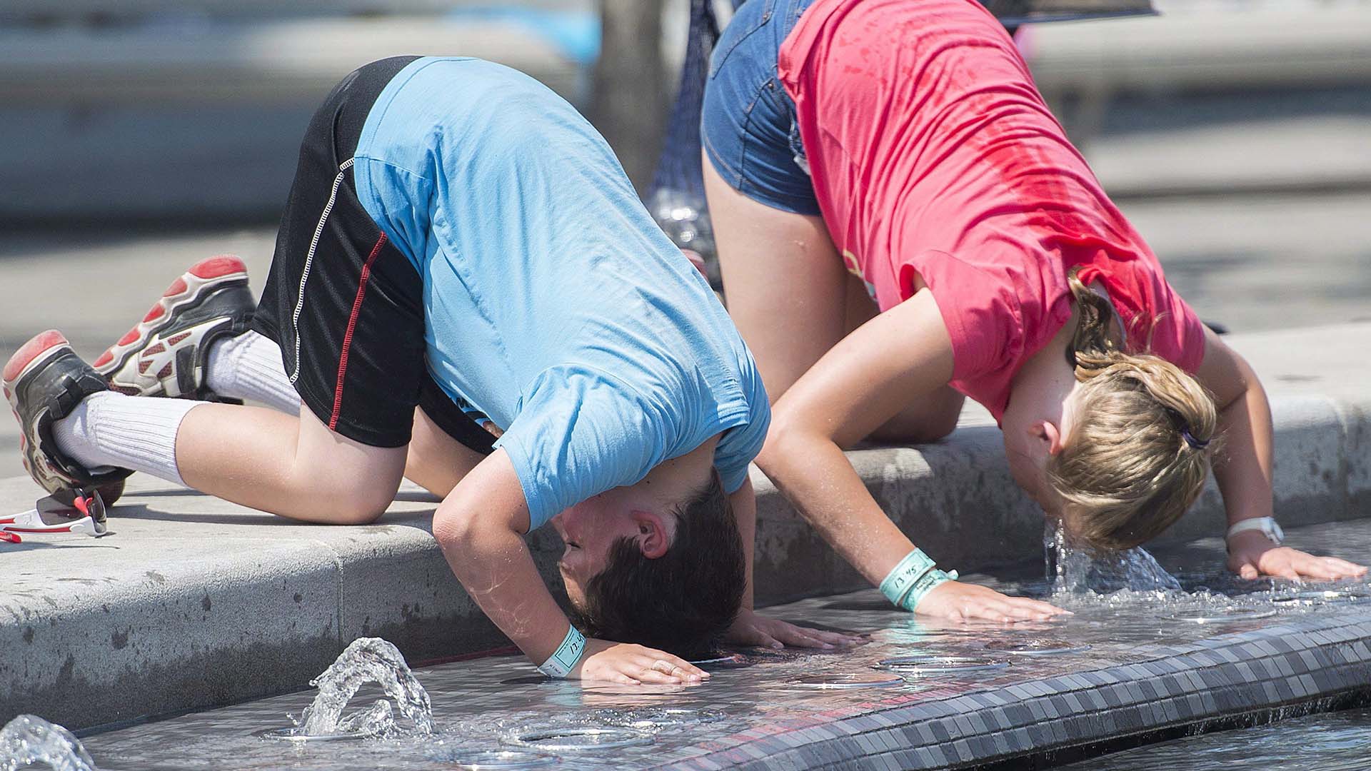 Un garçon et une fille se trempent la tête dans une fontaine d'eau lors d'une vague de chaleur à Montréal, en 2018.