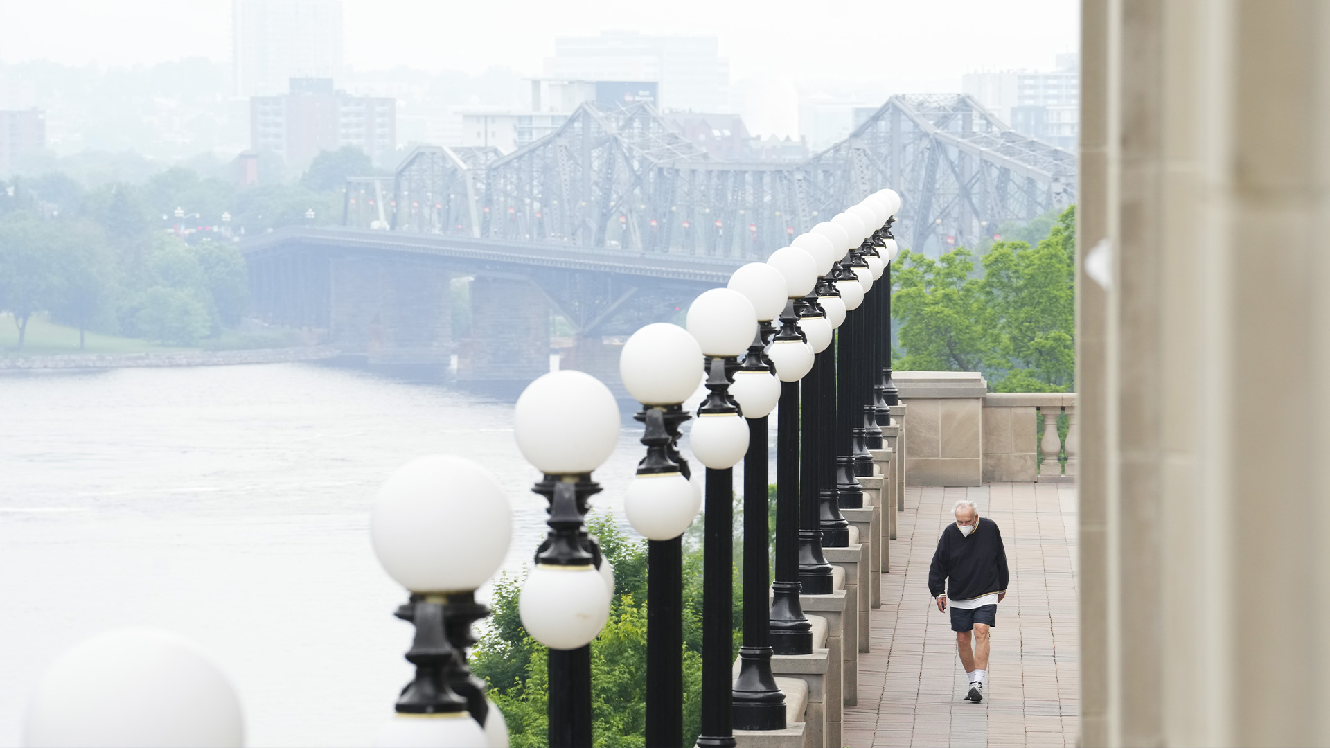 Une personne portant un masque traverse le centre-ville d'Ottawa le mercredi 7 juin 2023. La fumée d'un feu de forêt qui a déclenché des avis sur la qualité de l'air est visible au loin au-dessus de Gatineau, au Québec.