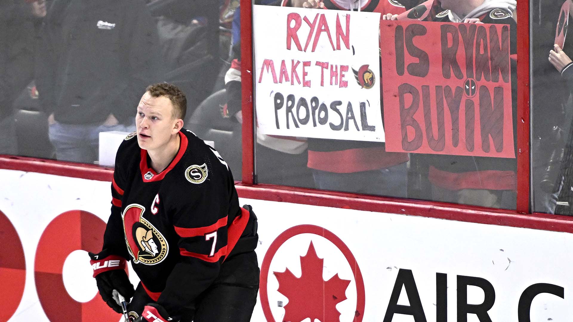 Brady Tkachuk lors d'un match des Sénateurs à Ottawa en novembre 2022. Des partisans lèvent des affiches pour demander à l'acteur Ryan Reynolds d'acheter l'équipe.