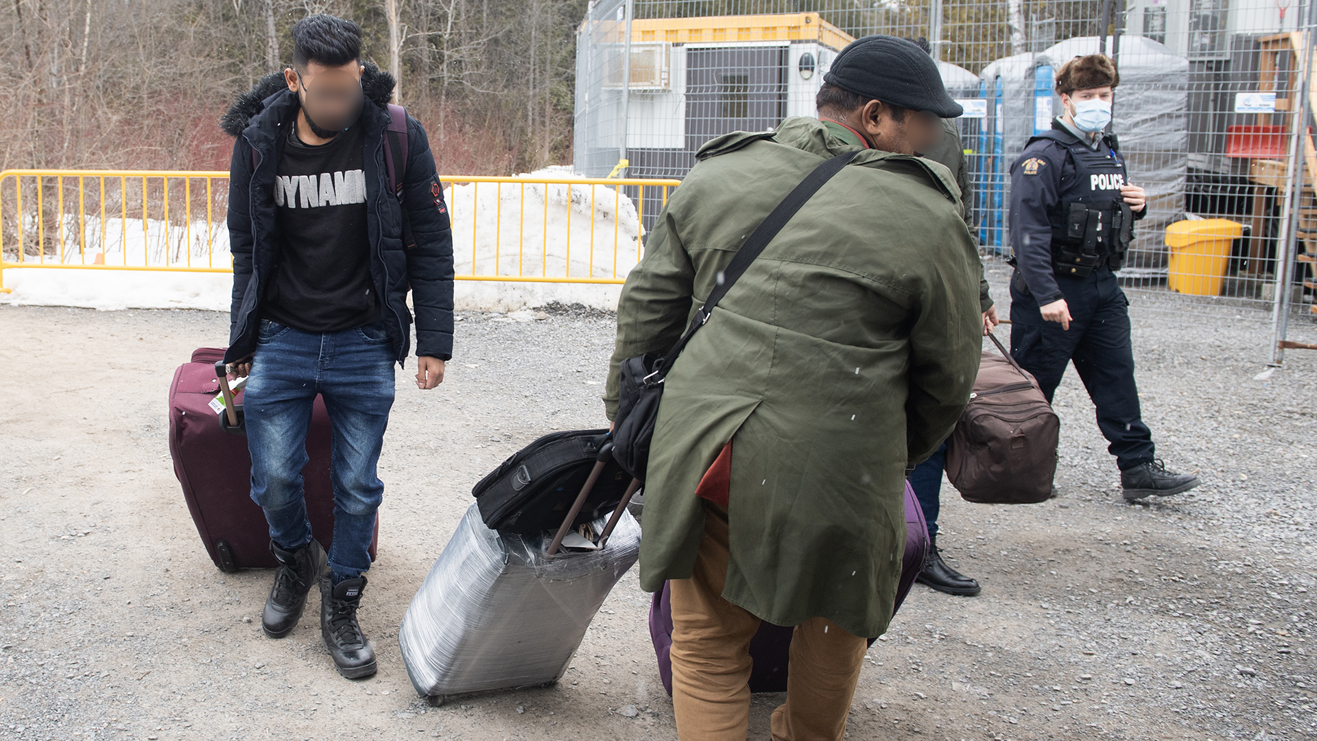 Des migrants entrent au Canada par le chemin Roxham sous les yeux d'un policier à Hemmingford, en mars 2023.