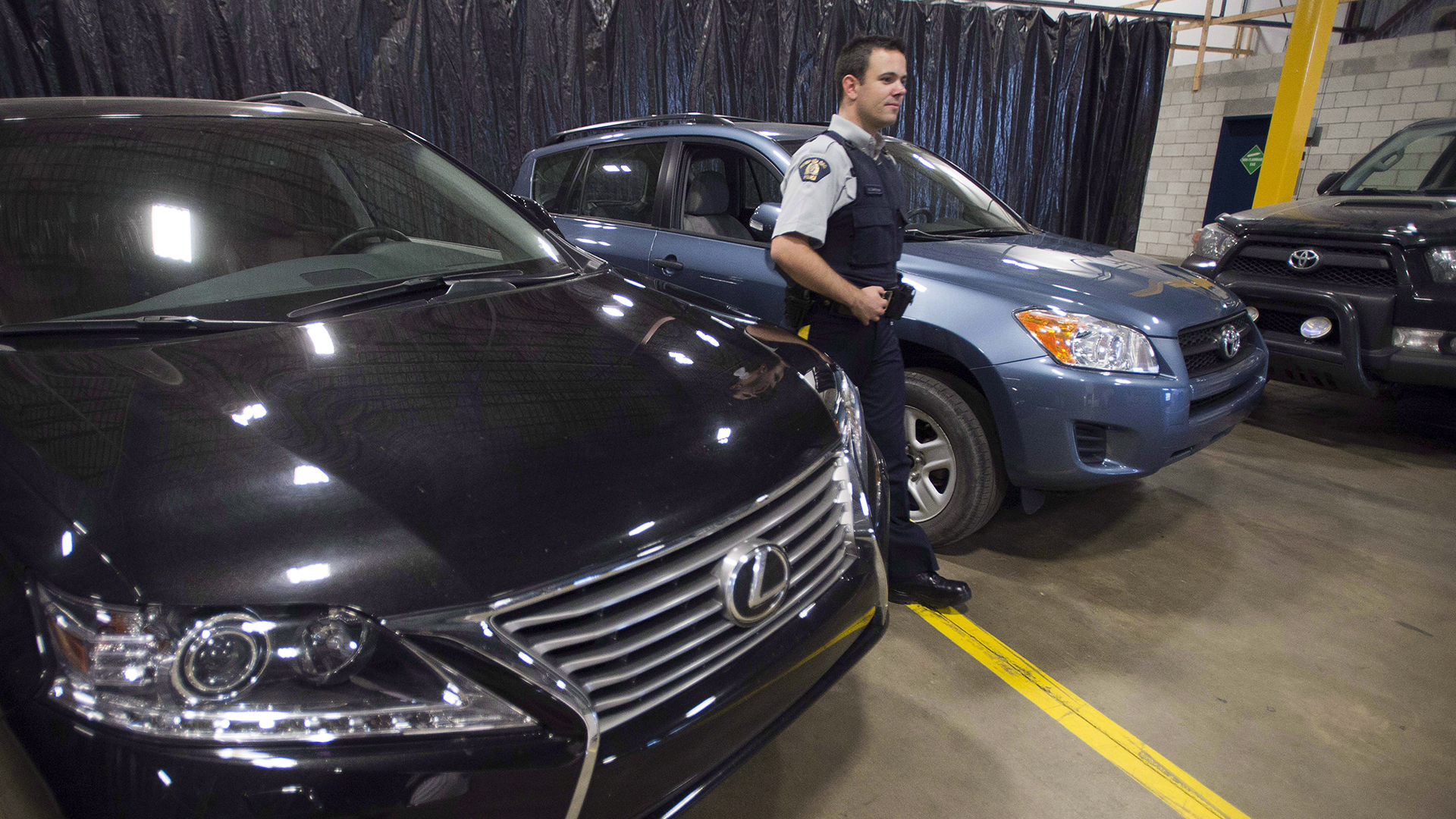 Un agent de la GRC examine des voitures volées récupérées à Montréal en juillet 2014.