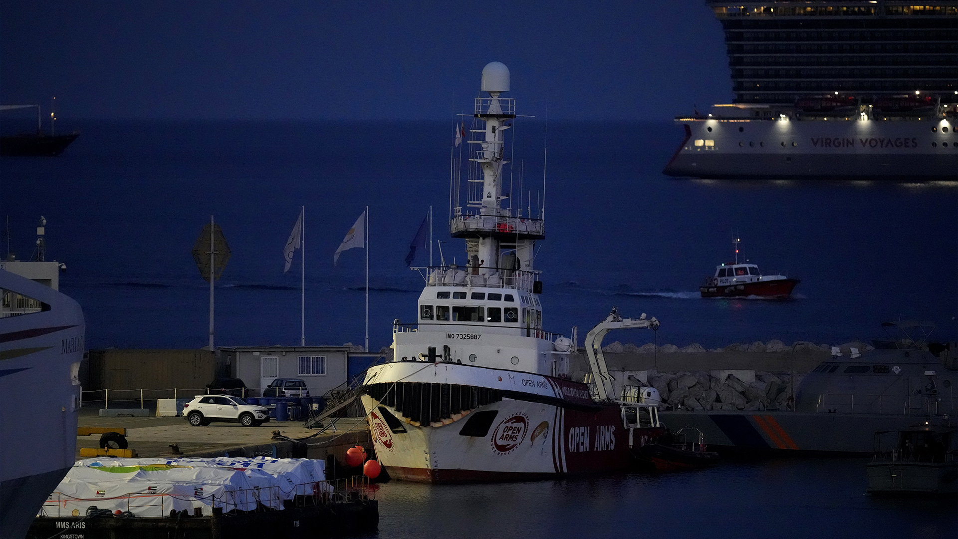 Des paquets d'aide sont vus à gauche, sur une plate-forme près du navire amarré appartenant au groupe d'aide Open Arms, alors qu'il se prépare à transporter quelque 200 tonnes de riz et de farine directement à Gaza, dans le port de Larnaca, à Chypre, le dimanche 10 mars 2024. 