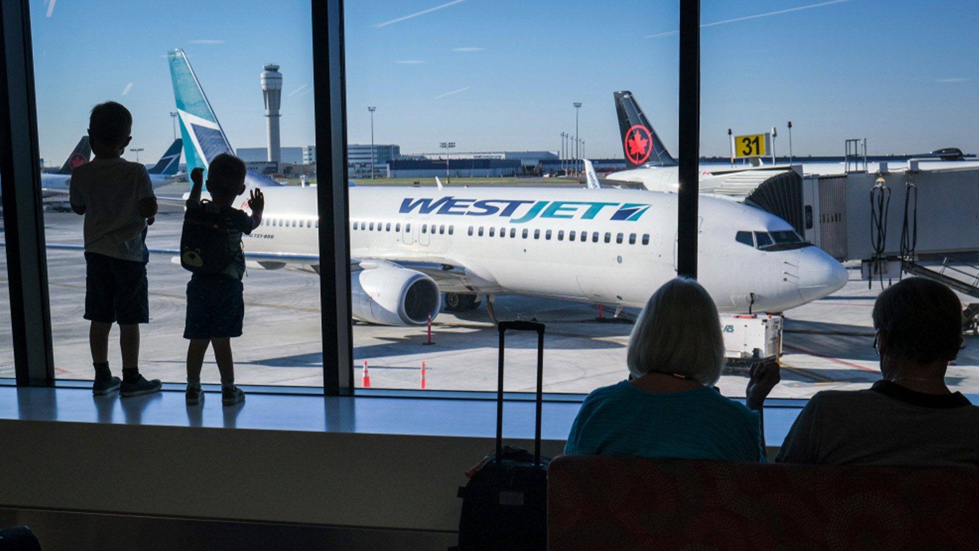 De jeunes garçons regardent les avions d'Air Canada et de WestJet à l'aéroport international de Calgary, en Alberta, le mercredi 31 août 2022. 