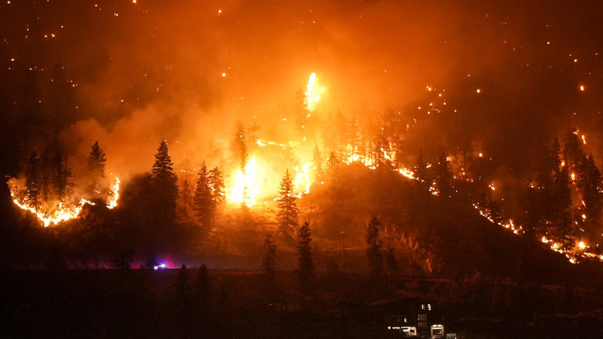 L'incendie de McDougall Creek brûle sur le flanc d'une montagne au-dessus d'une maison au bord d'un lac, à West Kelowna, en Colombie-Britannique, le vendredi 18 août 2023. 