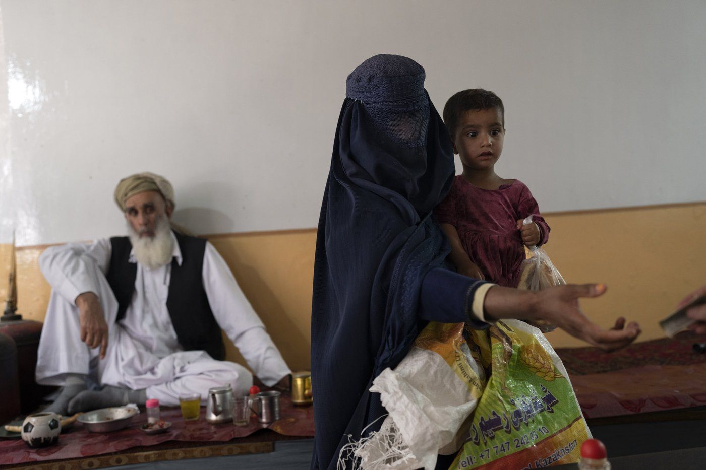 Une Afghane vêtue d'burqa mendie tout en portant sa fille dans un salon de thé de Kaboul, en Afghanistan, le 8 juin 2023. 
