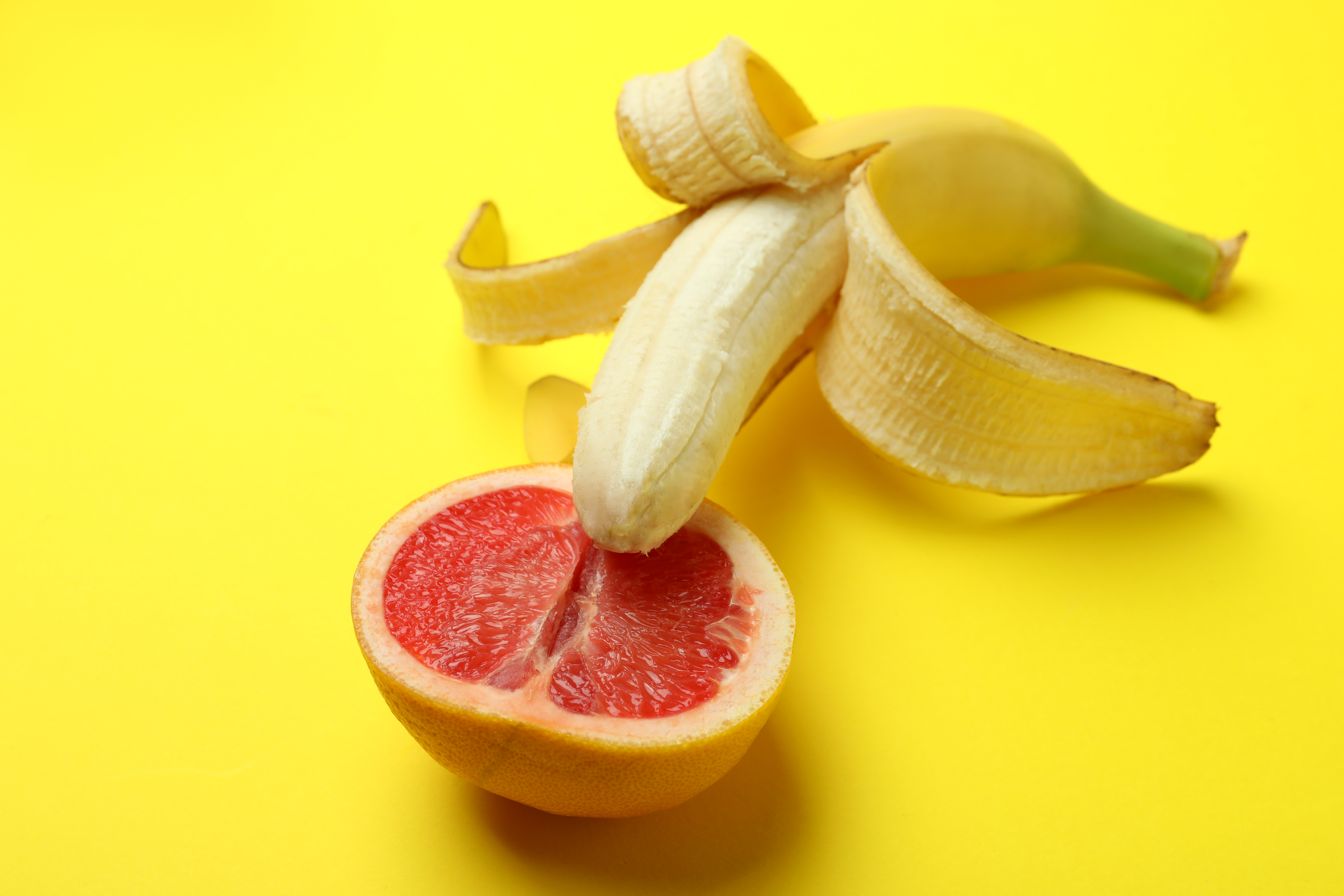 Banana with grapefruit half on yellow background