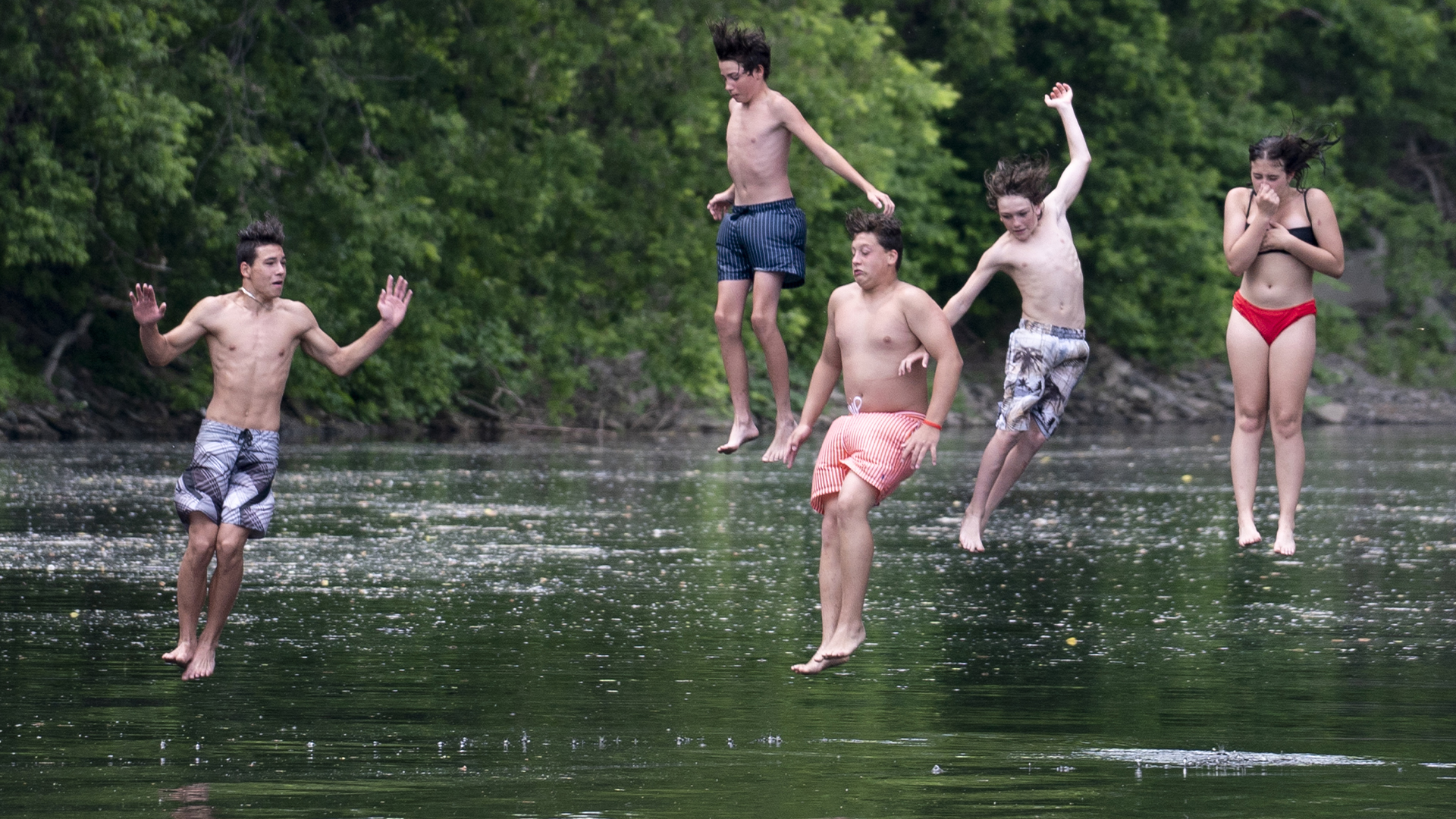 Un groupe de jeunes nageurs sautent d'un pont dans la rivière Assomption pour se rafraîchir de la chaleur estivale à Joliette, au Québec, le mardi 23 juin 2020.