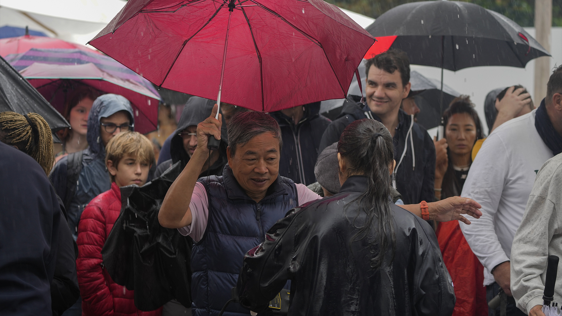 Des spectateurs munis d'un parapluie font la queue pour le contrôle de sécurité alors que la pluie retarde le début des matchs de la compétition de tennis, aux Jeux olympiques d'été de 2024, le samedi 27 juillet 2024, à Paris, en France. 