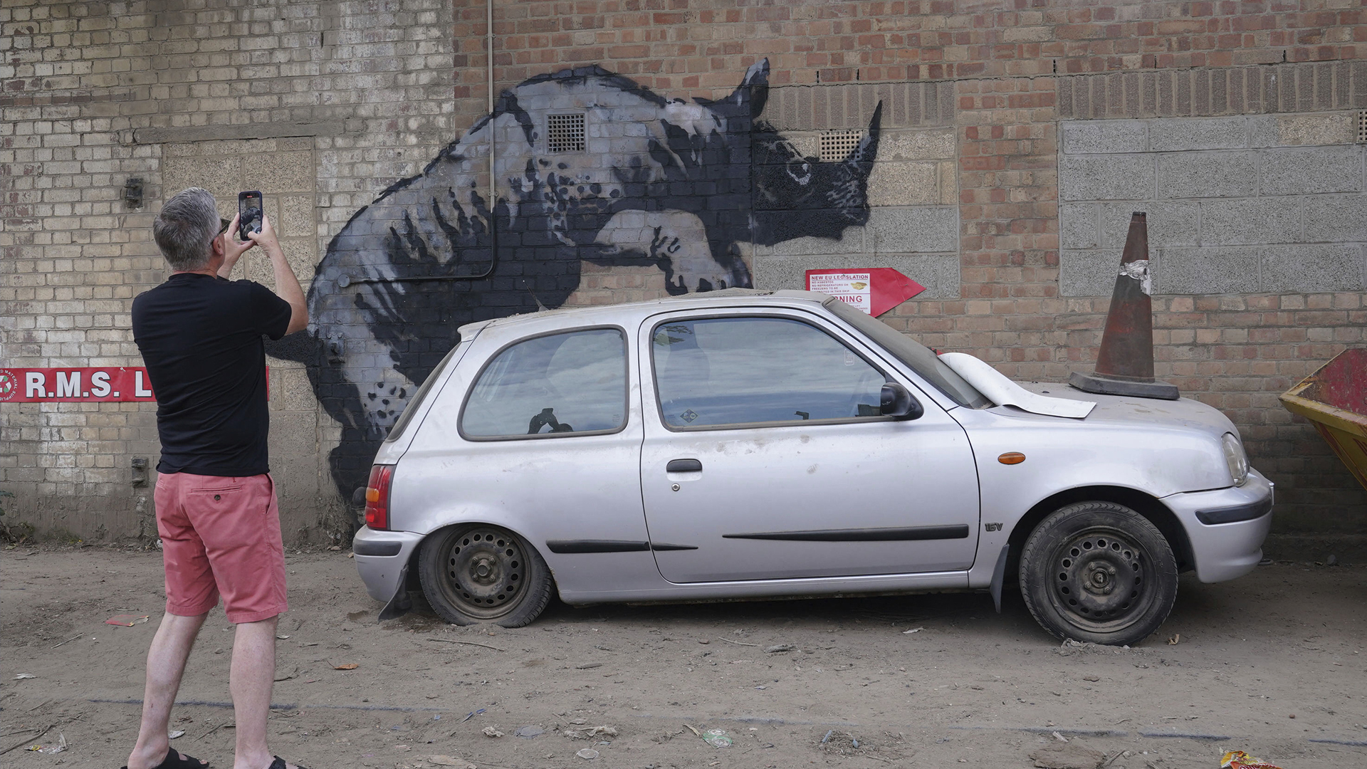 Un homme photographie une nouvelle œuvre d'art dévoilée par Banksy, représentant un rhinocéros qui semble grimper sur le toit d'une voiture, la huitième œuvre d'art de sa collection sur le thème des animaux, sur Westmoor Street à Charlton, au sud-est de Londres, lundi 12 août 2024. 