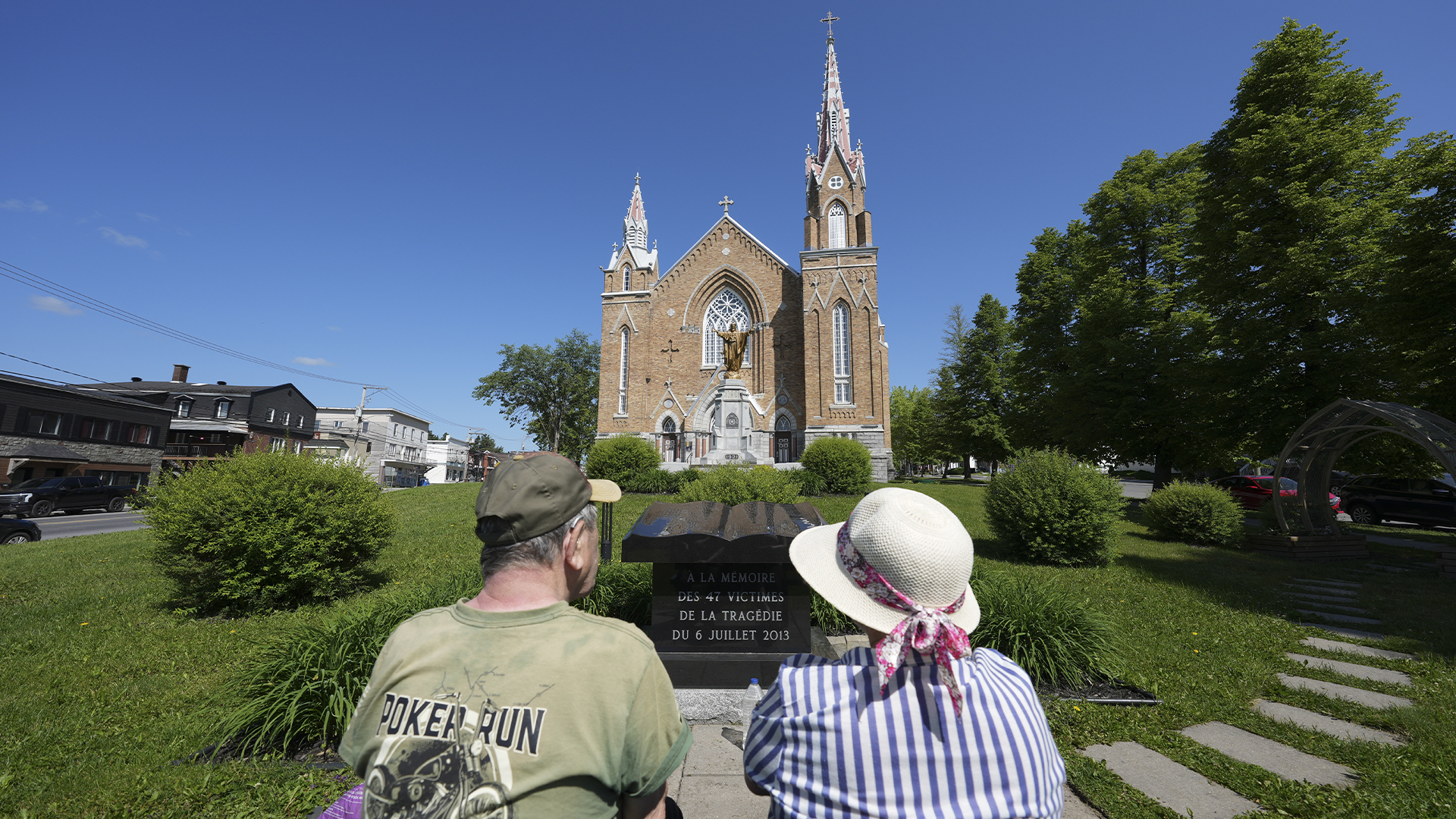 Des gens assis sur un banc face à l'église Sainte-Agnès de Lac-Mégantic le 22 juin 2023. 