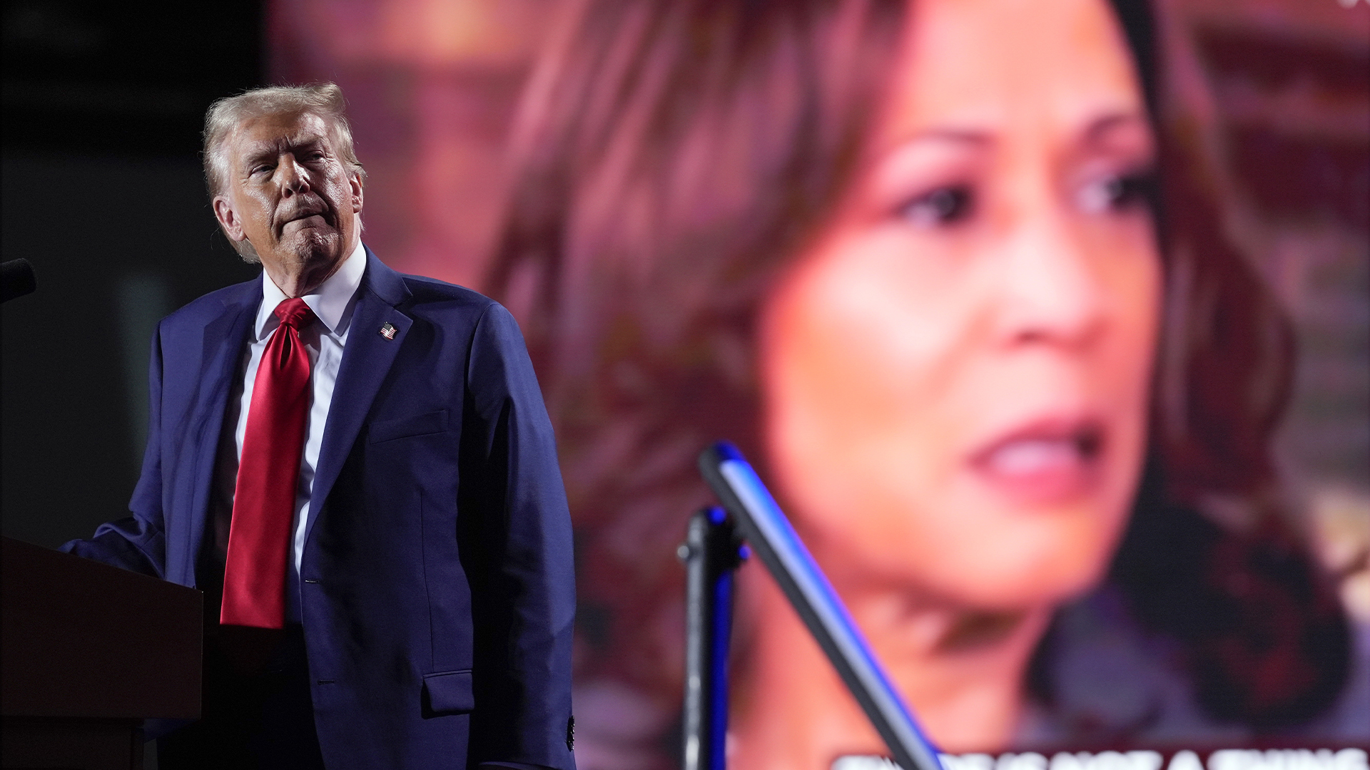 Le candidat républicain à l'élection présidentielle, l'ancien président Donald Trump, regarde une vidéo sur un écran avec la candidate démocrate à l'élection présidentielle, la vice-présidente Kamala Harris, alors qu'il s'exprime lors d'un événement de campagne, le vendredi 18 octobre 2024 à Detroit.