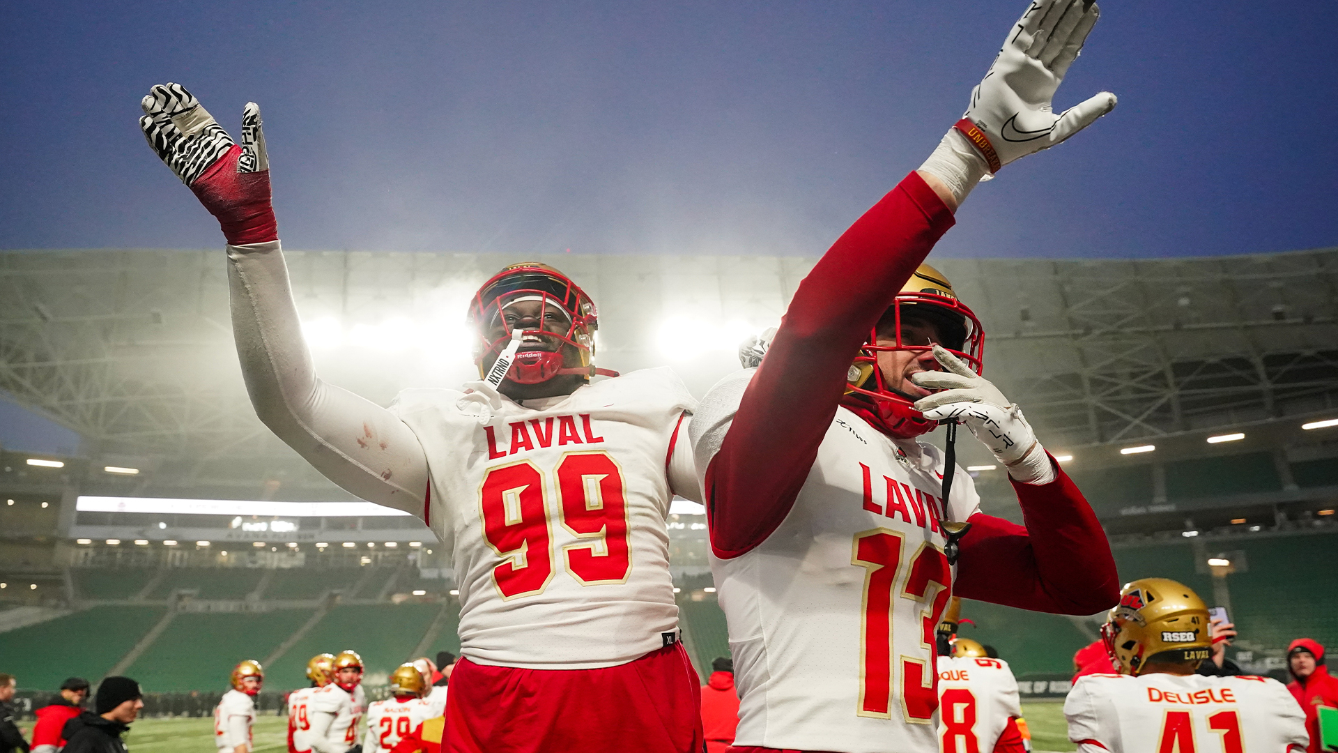 Le joueur de ligne défensive du Rouge et Or de l'Université Laval Yoann Miangué (99) et le demi-défensif du Rouge et Or de l'Université Laval Arnaud Laporte (13) saluent la foule pendant la deuxième demie du U Sports Mitchell Bowl contre les Rams de l'Université de Regina à Regina, le samedi 16 novembre 2024. 