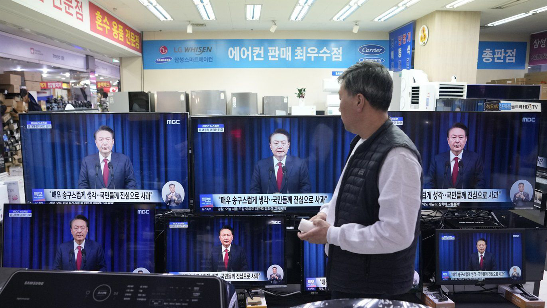 Un homme regarde les écrans de télévision montrant la diffusion de l'annonce du président sud-coréen Yoon Suk Yeol dans un magasin Yongsan Electronic à Séoul, en Corée du Sud, le samedi 7 décembre 2024.