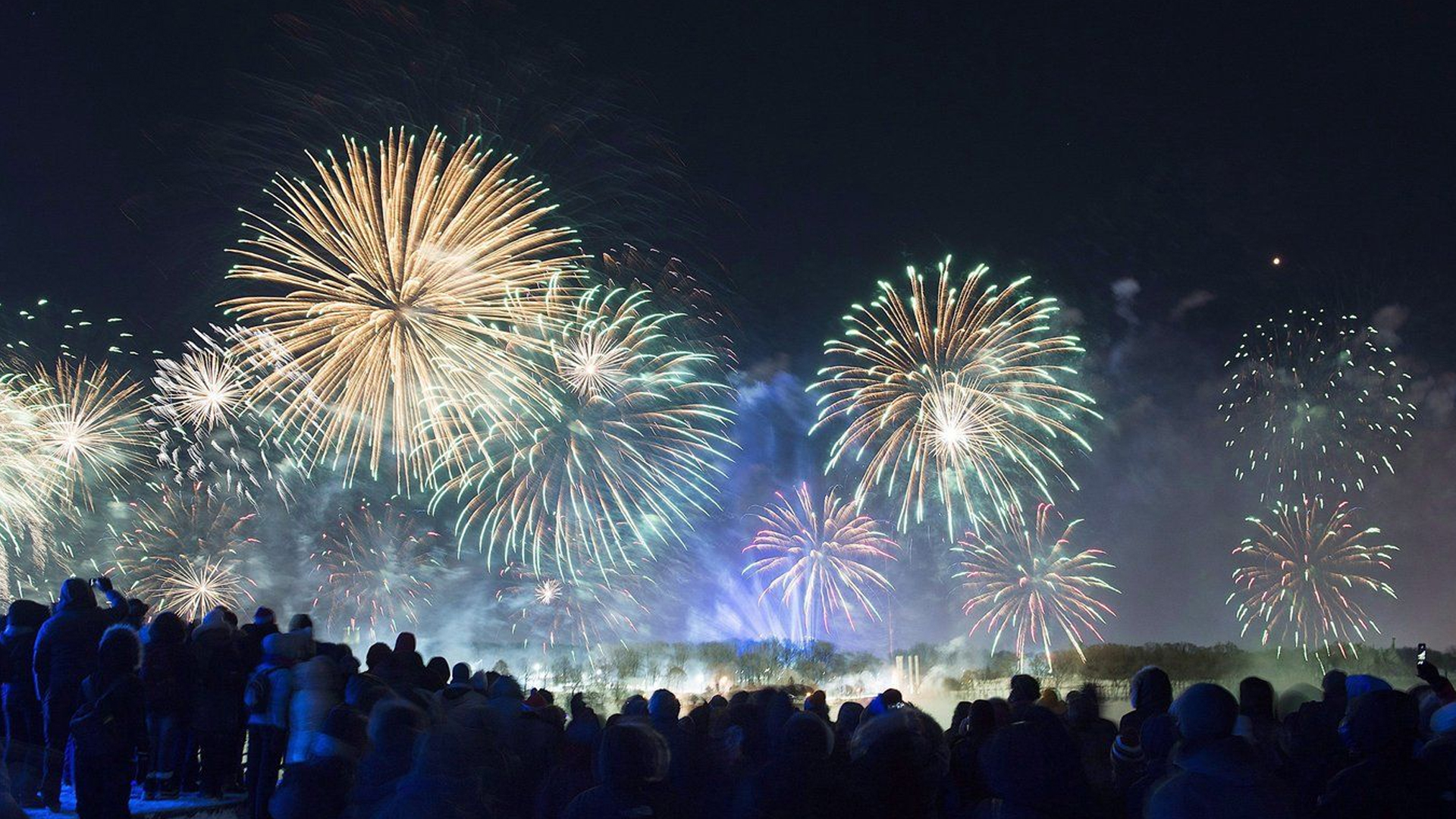 Les gens regardent les feux d'artifice qui explosent au-dessus du Vieux-Port de Montréal pendant les célébrations du Nouvel An, le lundi 1er janvier 2018.