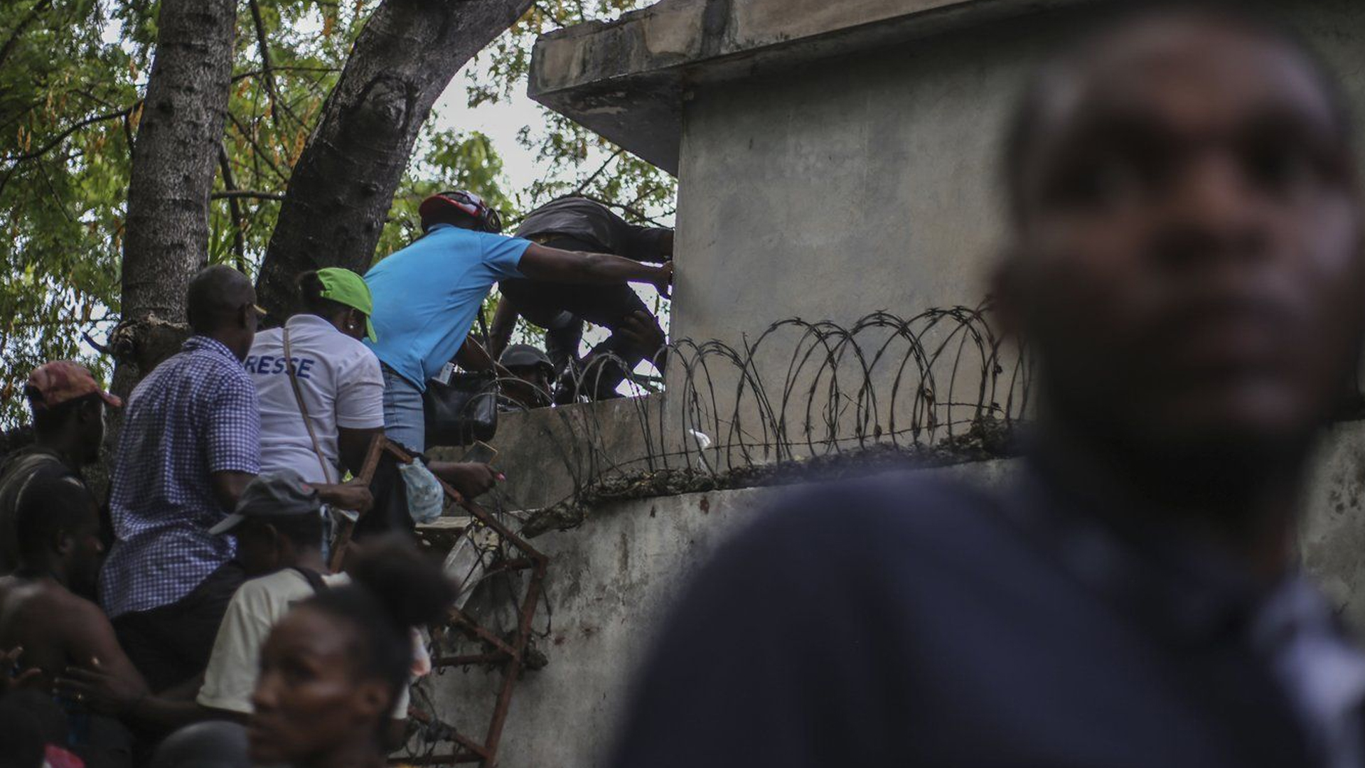 Des journalistes grimpent sur un mur pour se mettre à l'abri des tirs, après avoir été pris pour cible par des bandes armées à l'hôpital général de Port-au-Prince, en Haïti, le mardi 24 décembre 2024.