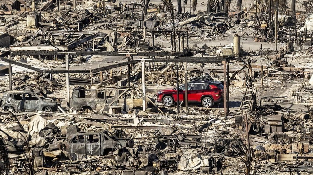 Une voiture passe devant des maisons et des véhicules détruits par l'incendie de Palisades au Pacific Palisades Bowl Mobile Estates, le 12 janvier 2025, à Los Angeles.