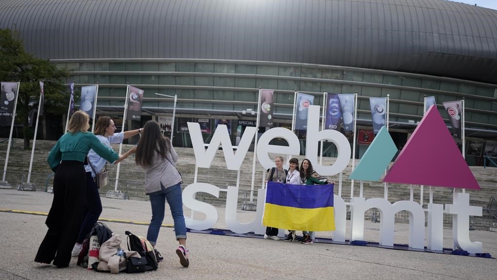 Des personnes posent avec un drapeau ukrainien près du logo de la conférence technologique Web Summit à l'extérieur du lieu qui l'accueille à Lisbonne, mercredi 2 novembre 2022. 