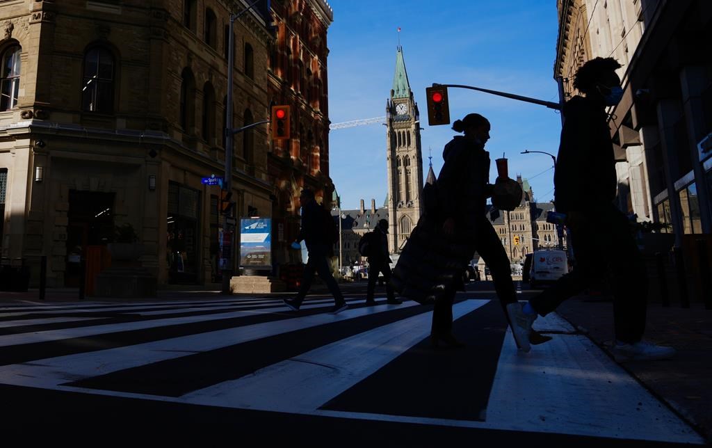 The Canada Flag flies on the Peace Tower of Parliament Hill as pedestrians make their way along Sparks Street Mall in Ottawa on Tuesday, Nov. 9, 2021. Federal public servants are expected to be back in office by the end of the month. THE CANADIAN PRESS/Sean Kilpatrick