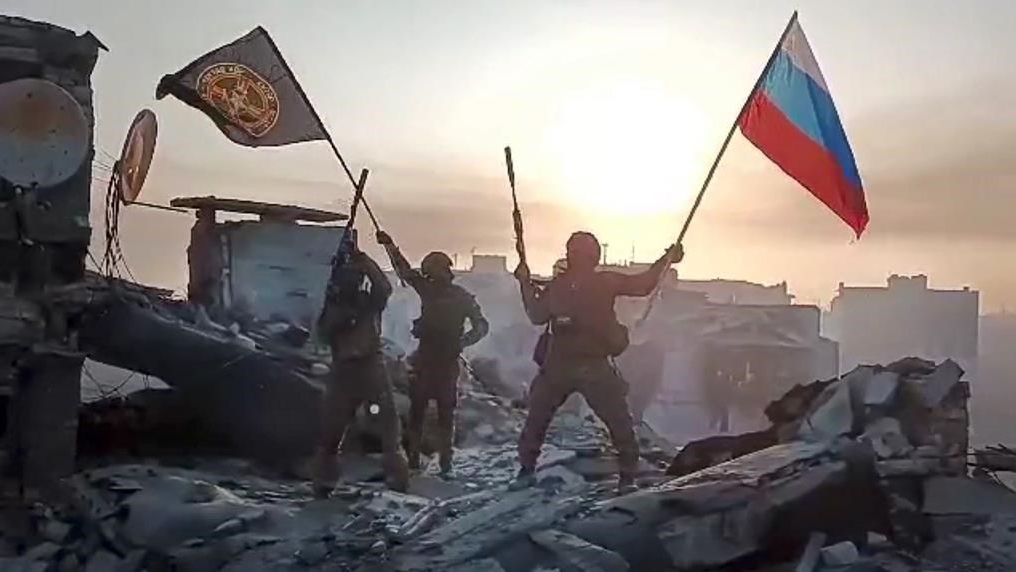 Les forces du groupe Wagner brandissent des drapeaux russes et Wagner au sommet d'un bâtiment endommagé à Bakhmut, en Ukraine.