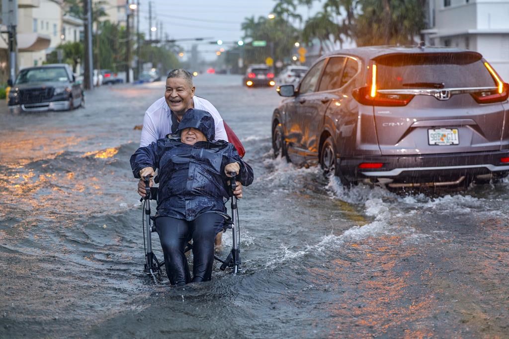 Victor Corone, 66, pushes his wife Maria Diaz, 64, in a wheelchair through more than a foot of flood water on 84th street in Miami Beach, Fla. on Wednesday, June 12, 2024. The annual rainy season has arrived with a wallop in much of Florida, where a disorganized disturbance of tropical weather from the Gulf of Mexico has caused street flooding and triggered tornado watches but so far has not caused major damage or injuries. (AL Diaz/Miami Herald via AP)